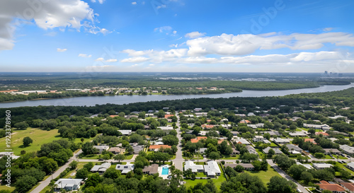 High angle aerial view of a green suburban neighborhood with a wide river and blue sky