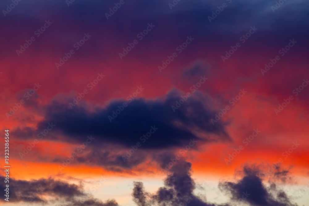 Fototapeta premium Vibrant orange and red clouds stretch across a dark blue sky
