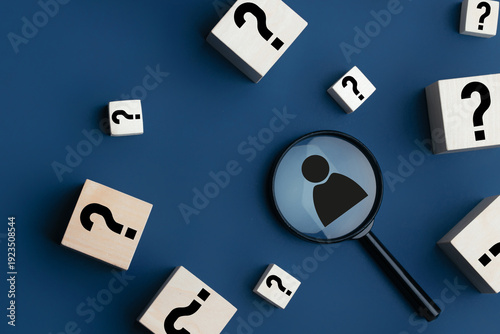 Magnifying glass focusing on a person icon surrounded by wooden blocks with question marks on a blue background, symbolizing inquiry and search for identity