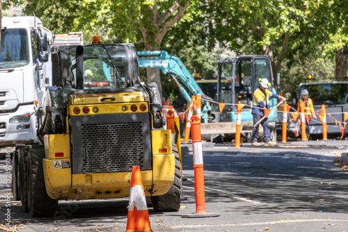 Slika na platnu Road construction work in progress on an urban street with a road roller and workers in safety gear installing new asphalt
