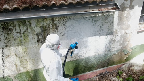 Obraz na płótnie Worker in white hazmat suit and full-face respirator using handheld electric spr