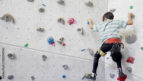 Foto Young boy climbing an indoor artificial wall in harness and climbing shoes, buil