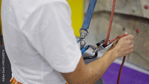 Photos Person preparing for indoor rock climbing, hands adjusting belay device with rop