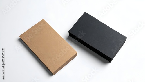 Two rectangular boxes, one beige, one black, laying on a white surface
