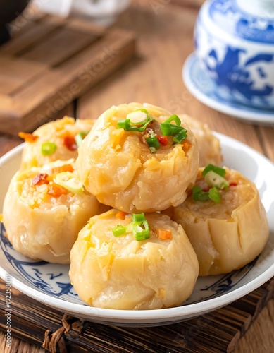 Steamed dumplings piled on a patterned plate, garnished with green onions, in a warm, inviting, close-up food shot