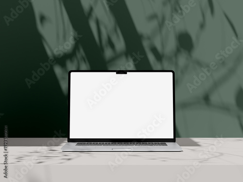 Modern laptop mockup with blank white screen on white table with organic plant shadows