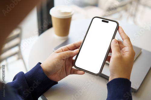 Hands using a smartphone with an empty screen at a cozy cafe table, ideal for concepts of mobile technology, remote work, or everyday digital.