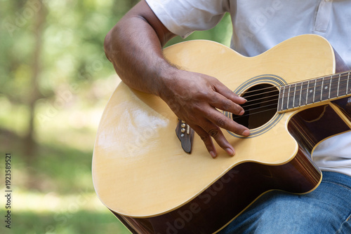 Close up of male musician hand playing acoustic guitar in green nature garden. Man performing music outdoors with wooden instrument for leisure, relaxation and artistic lifestyle concept.