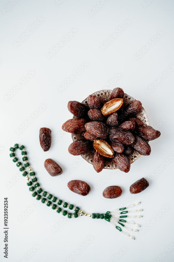 Fototapeta premium Minimalistic flat lay with a bowl of dates and green prayer beads chain
