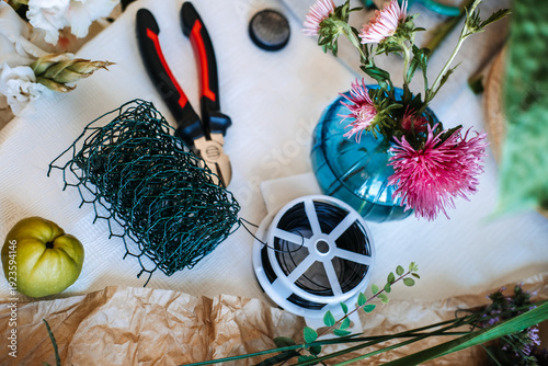 High angle view of florist tools and materials including wire mesh and flowers on table. Eco-friendly floristry, sustainable floral design, chicken wire technique, plastic-free mechanics.
