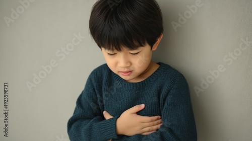Young Korean boy suffering from stomach ache holding his belly with a painful expression.