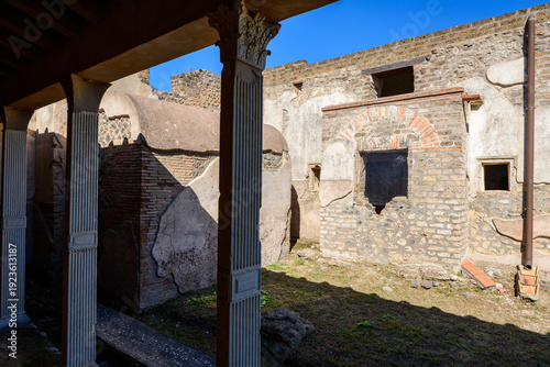 Foto Bright sunlight casts sharp shadows across the fluted columns and weathered stone walls of the House of Julia Felix in Pompeii, Italy