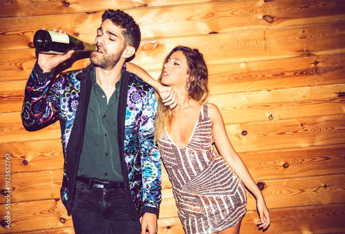 Young woman leaning on male friend drinking champagne against wall in party