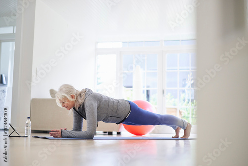 Active senior woman practicing plank position on mat at home
