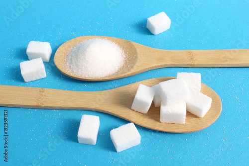 Bild auf Leinwand On a blue background, on wooden spoons, there are two types of sugar, loose and cubed