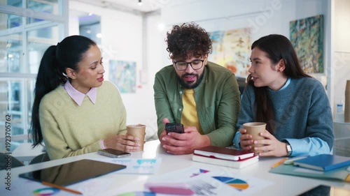 Office colleagues sitting at desk with coffee cups and notebooks. Group workers browsing news on smartphone. Male employee holding mobile and scrolling screen. Team discussing updates during break.