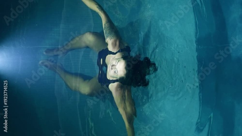 Woman with tattoos floating and submerging in a swimming pool at night