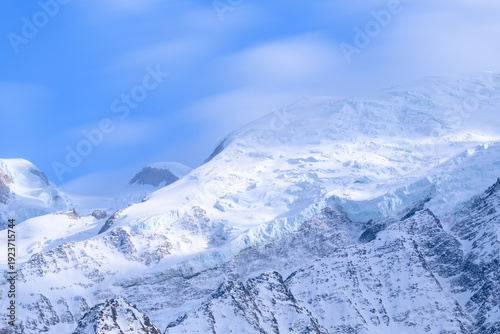 Bright sunlight highlights the intricate glacier formations and snow-covered slopes of Mont Blanc, set against a vivid blue sky for a crisp, tranquil alpine scene.