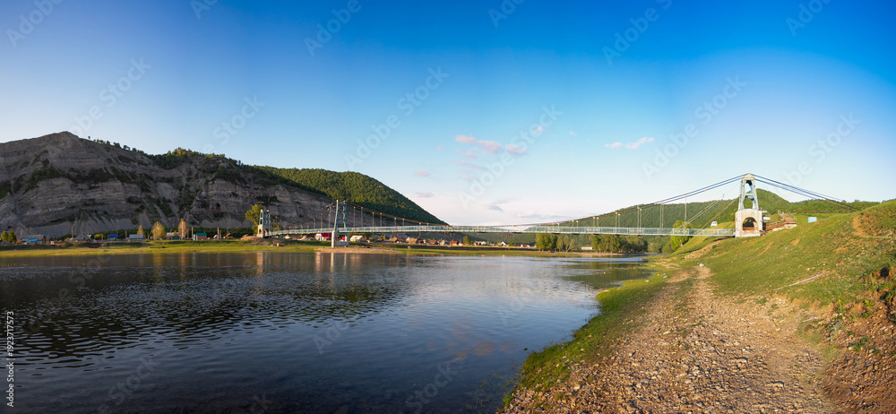 Obraz premium Southern Urals, Bashkortostan, suspension bridge in the village of Tash-Asty. The Zilim River and the Ukly Kaya rock.