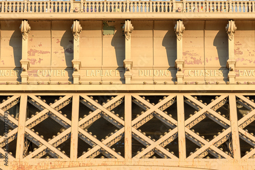 Obraz na płótnie Close-up of the Eiffel Tower's first level featuring engraved scientist names, ornate columns, and diagonal iron crossbeams bathed in warm golden sunlight