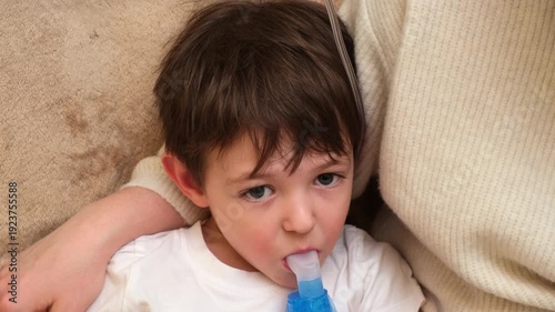 Child receiving nebulizer treatment from a womans hand for asthma or respiratory illness. Inhalation therapy concept for kid health.
