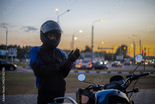 A woman on a motorcycle wearing a helmet and a motorcycle jacket in the evening in the city