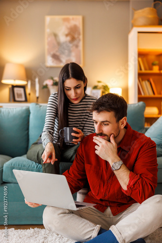 Couple searching for vacation online booking ideas using laptop computer while relaxing at home