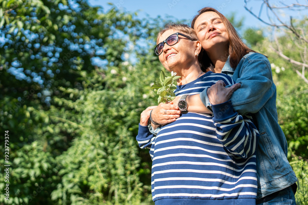 Naklejka premium Tender hug between a happy senior mother and her adult daughter in a spring garden on Mother's Day.