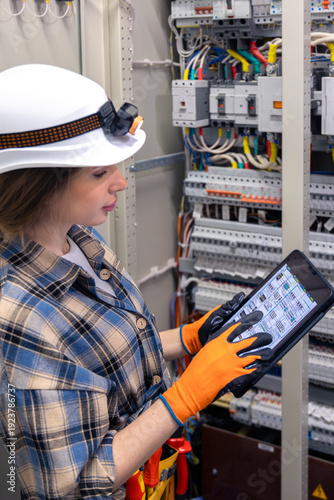 Obraz na płótnie Woman engineer uses tablet beside open switchboard. Schematic screen.