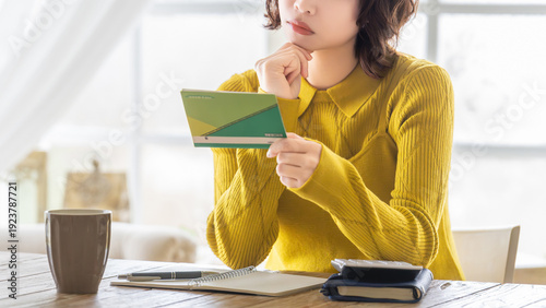 Photos 銀行の預金通帳を確認する女性, Woman checking a bank passbook at home