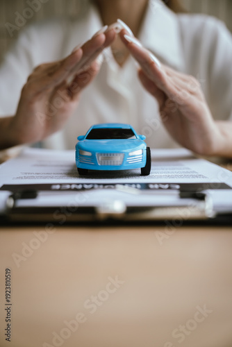 Hands protect two toy cars placed on a car insurance document, symbolizing vehicle protection, accident coverage, and auto insurance policy planning.