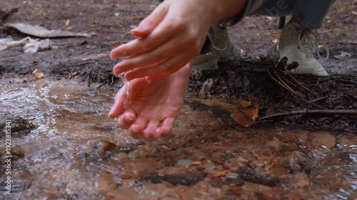 Close-up of female hands scooping and washing with cool, clear water from a natural stream flowing through a forest, embodying a concept of purity, nature, and refreshment