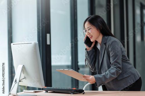 Asian businesswoman engaging in a phone conversation while reviewing documents, reflecting communication and multi tasking in her professional career