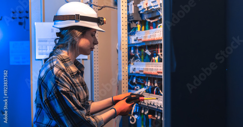Woman electrician repairs electrical panel in technical room. Panel maintenance.