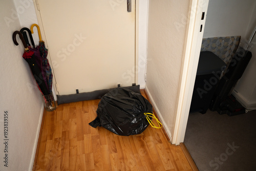 Full black trash bag on the corridor floor next to an interior door in a casual home setting. Domestic scene waste management and household routine. Concept of cleaning, domestic, organization.