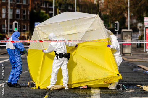 Three forensics officers position an examination tent over a crime scene to preserve evidence prior to a detailed examination. 