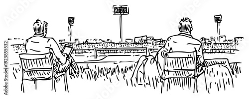 Two people sitting on benches using a digital tablet at a sports field under floodlights