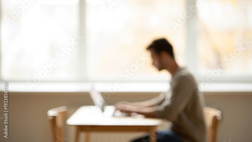 Young man using laptop in a blurry, out of focus indoor working or studying environment at home