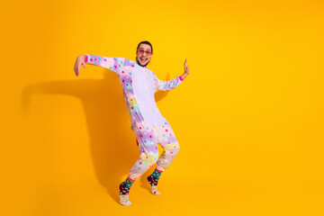 Playful man in a colorful unicorn pajama jumpsuit dancing against a bright yellow background for a fun lifestyle stock photo that captures joy energy