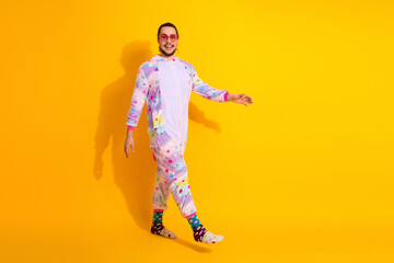 Joyful man in pastel unicorn pajamas walks against bright yellow background in a fun playful jumpsuit stock photo