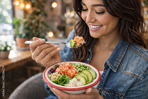 Smiling woman eating salmon poke bowl with avocado in cozy cafe