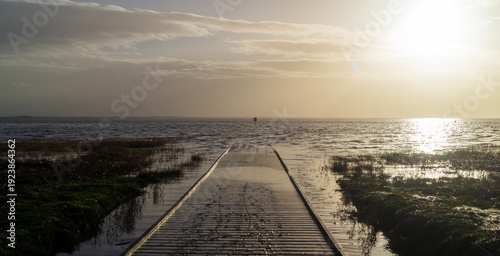 Wooden pier covered with water and sand against the backdrop of the sea with sunlight from the side
