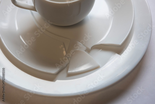 Cup sits on broken plate on table with white surface during bright day