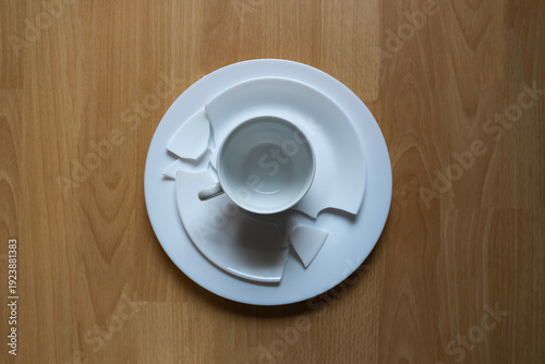 Cup and plate break on wooden table during afternoon snack time with scattered pieces all around