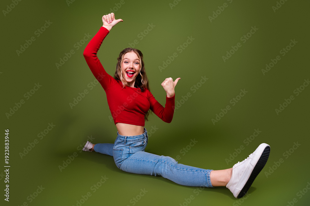 Fototapeta premium Young woman in red crop top sits on green backdrop smiling with energy and excitement