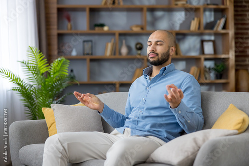 Εκτύπωση καμβά Young man practicing mindfulness meditation on a comfortable sofa in his living