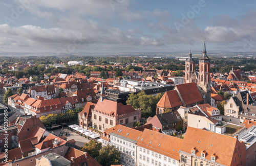 Aerial drone view of Goettingen (Göttingen) old town in Germany, featuring red-roofed historic buildings and church towers, with a small statue visible near a public square under a partly cloudy sky.