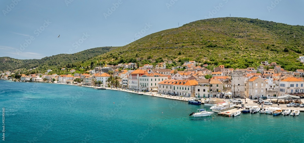 Naklejka premium Croatia's island of Vis in Dalmatia. The historic town of Vis on a summer day. Mountains and forests, and the azure Adriatic Sea. Houses and church towers.