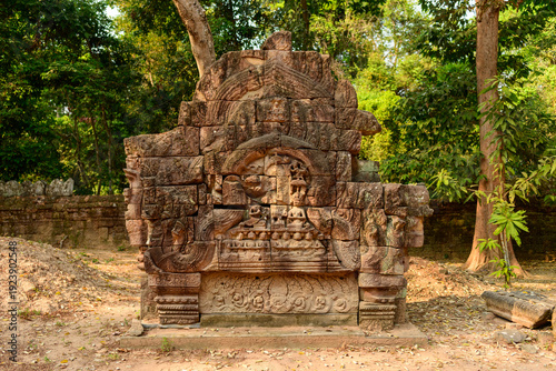 Intricately carved sandstone lintel stands amid the forest at Ta Som temple in Cambodia's Angkor region. Warm sunlight highlights the detailed bas-relief and weathered stone against a backdrop of