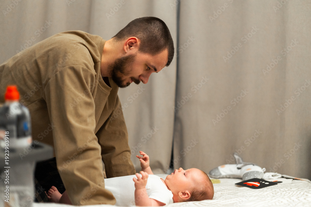 Fototapeta premium Father gently looking down at his newborn baby lying on a changing table